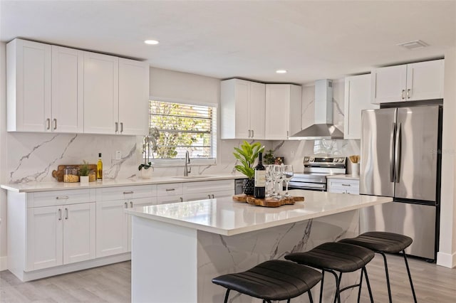 kitchen featuring stainless steel appliances, light wood-style flooring, a sink, and wall chimney range hood