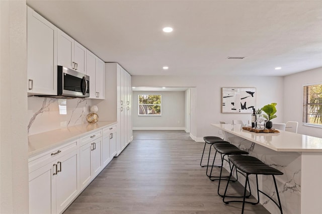 kitchen with recessed lighting, a breakfast bar, stainless steel microwave, baseboards, and white cabinetry