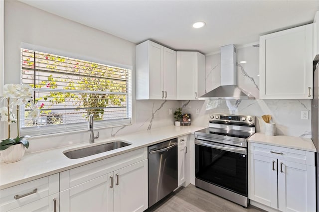kitchen featuring light countertops, wall chimney range hood, appliances with stainless steel finishes, and a sink