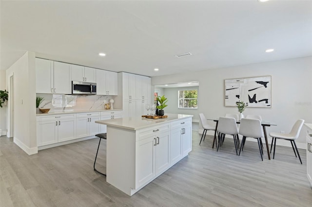 kitchen with a center island, light wood-style flooring, stainless steel microwave, recessed lighting, and light countertops