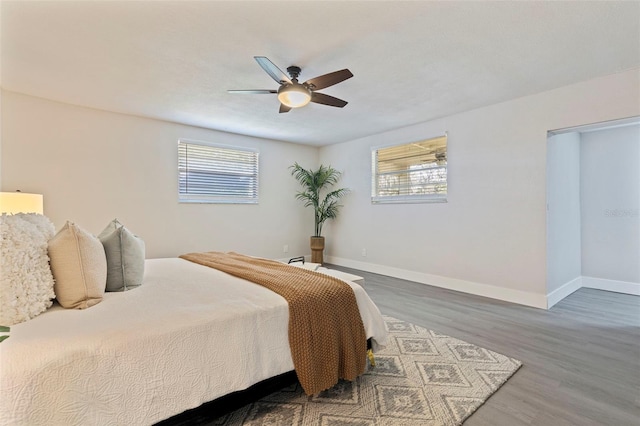 bedroom featuring baseboards, a ceiling fan, wood finished floors, and multiple windows