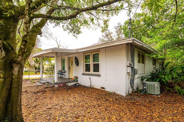 single story home featuring covered porch, fence, central AC unit, and stucco siding