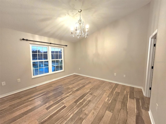 spare room with baseboards, dark wood-type flooring, and a notable chandelier