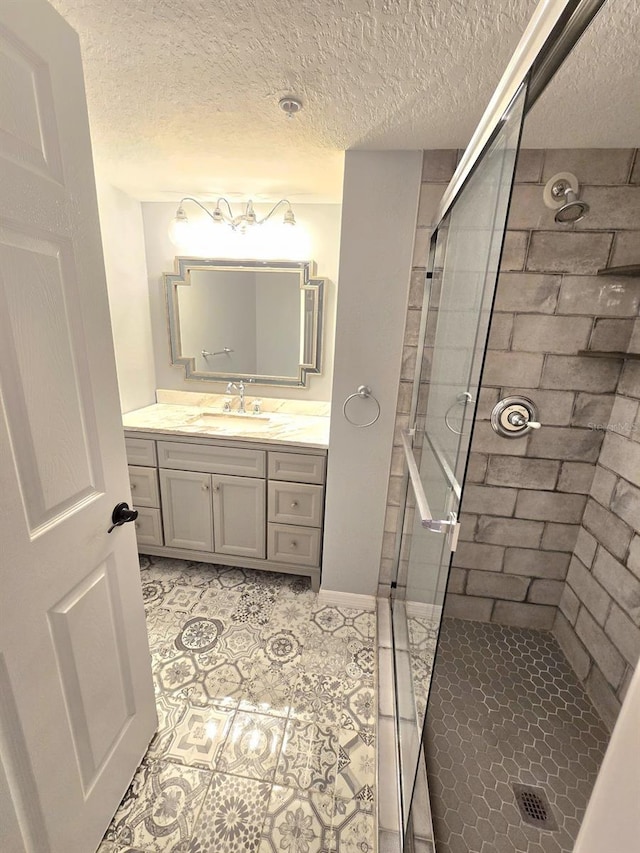 bathroom with a textured ceiling, tiled shower, and vanity