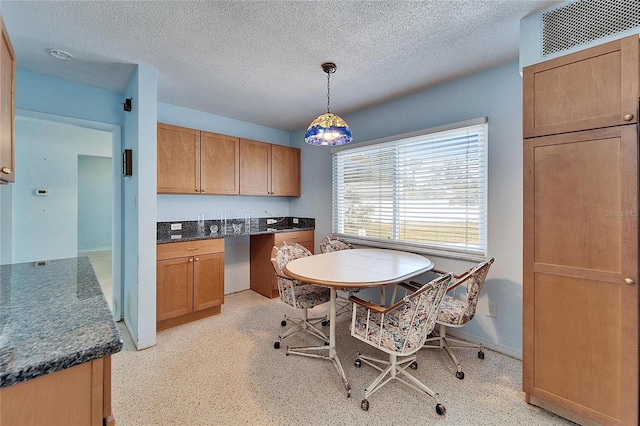 kitchen with baseboards, brown cabinets, decorative light fixtures, a textured ceiling, and built in desk