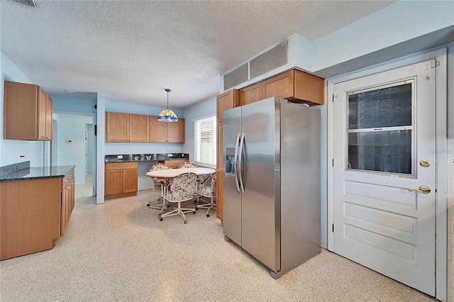 kitchen featuring hanging light fixtures, light speckled floor, brown cabinetry, and stainless steel fridge with ice dispenser