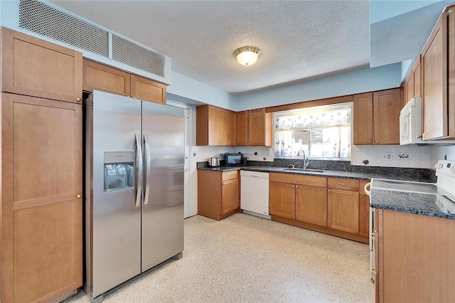 kitchen featuring a textured ceiling, white appliances, a sink, and brown cabinets