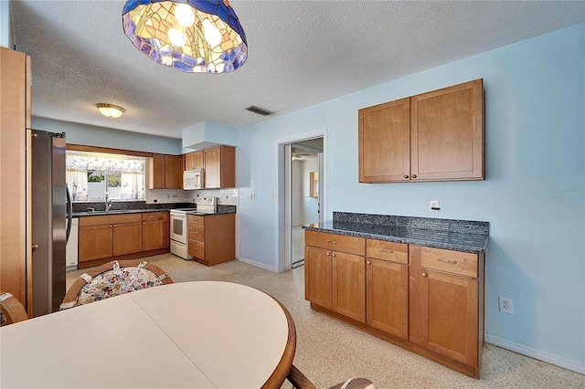 kitchen with brown cabinets, visible vents, a sink, white appliances, and baseboards