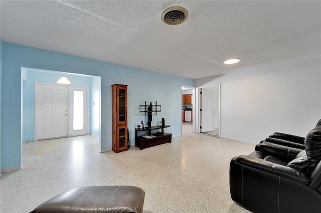 living area featuring baseboards, visible vents, a textured ceiling, and speckled floor