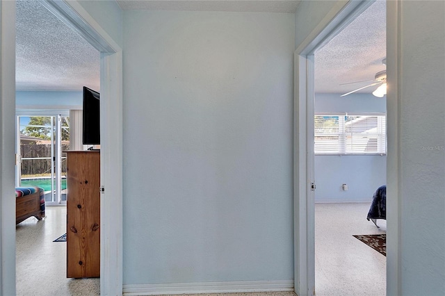 corridor with a textured ceiling, plenty of natural light, and baseboards