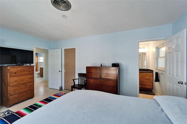 bedroom featuring connected bathroom, visible vents, and a textured ceiling