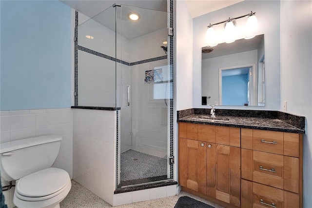 bathroom with a stall shower, vanity, toilet, and tile walls