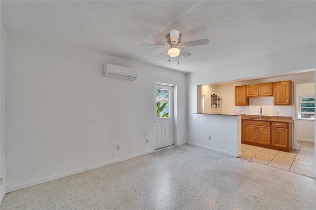 kitchen with a wall unit AC, ceiling fan, a textured ceiling, light speckled floor, and a sink