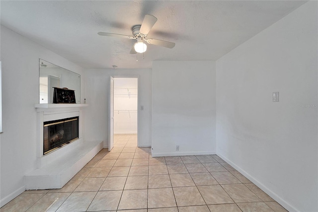 unfurnished living room featuring light tile patterned flooring, baseboards, a ceiling fan, and a glass covered fireplace