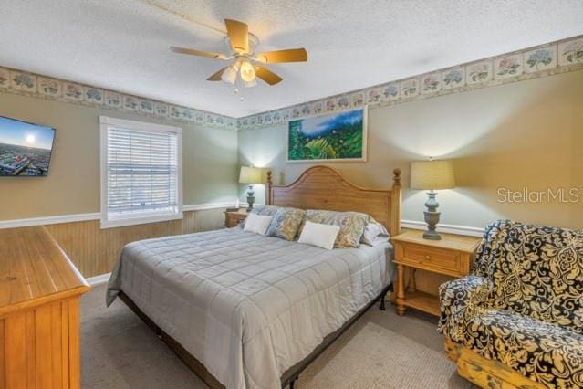 bedroom featuring ceiling fan, a textured ceiling, wood walls, wainscoting, and carpet