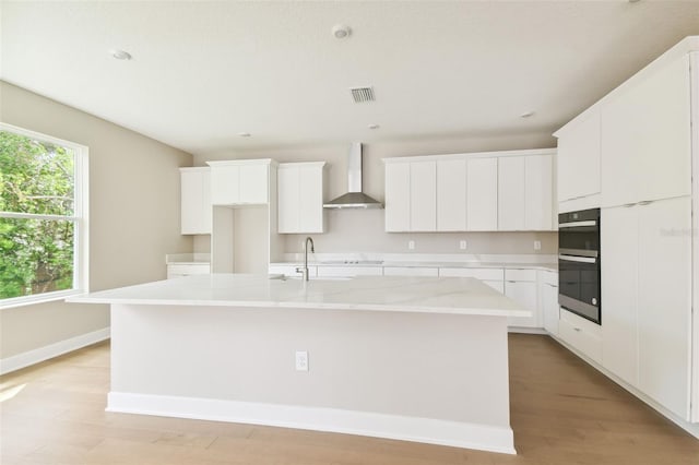 kitchen featuring a center island with sink, visible vents, double oven, a sink, and wall chimney exhaust hood