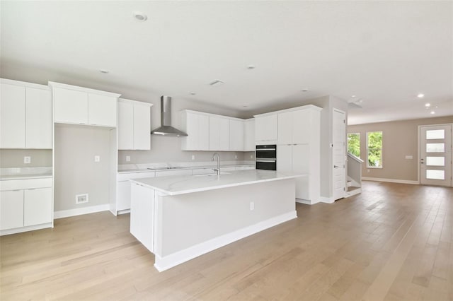 kitchen with wall chimney range hood, light wood-style flooring, white cabinets, and light countertops