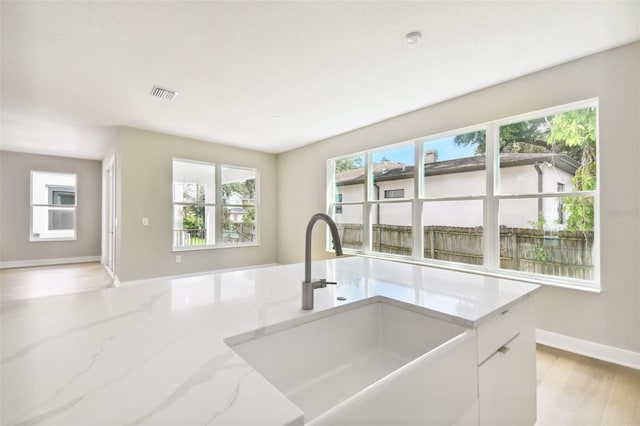 kitchen featuring light stone counters, visible vents, white cabinets, a sink, and baseboards