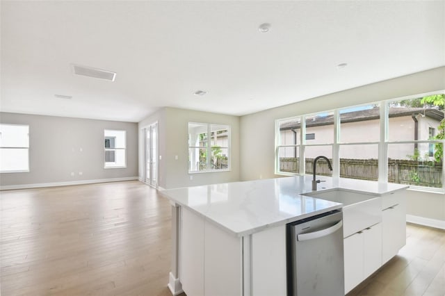 kitchen featuring a center island with sink, light wood finished floors, stainless steel dishwasher, open floor plan, and a sink