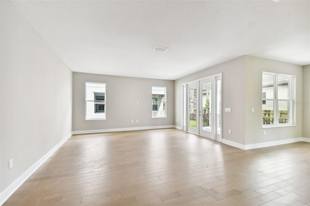 spare room featuring french doors, visible vents, light wood-style flooring, a textured ceiling, and baseboards