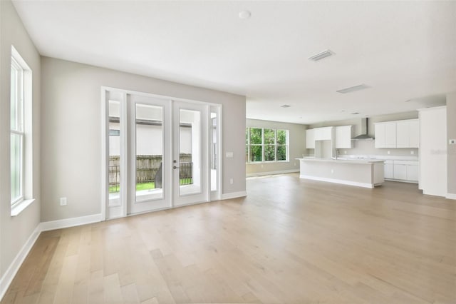 unfurnished living room featuring light wood-type flooring, visible vents, and baseboards