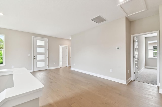 unfurnished living room featuring baseboards, light wood finished floors, visible vents, and attic access