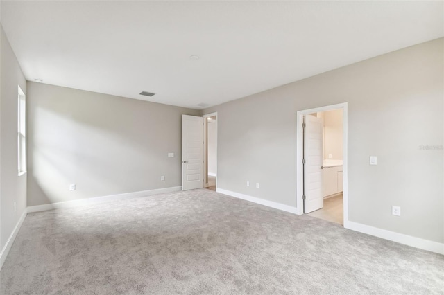 spare room featuring light carpet, visible vents, and baseboards