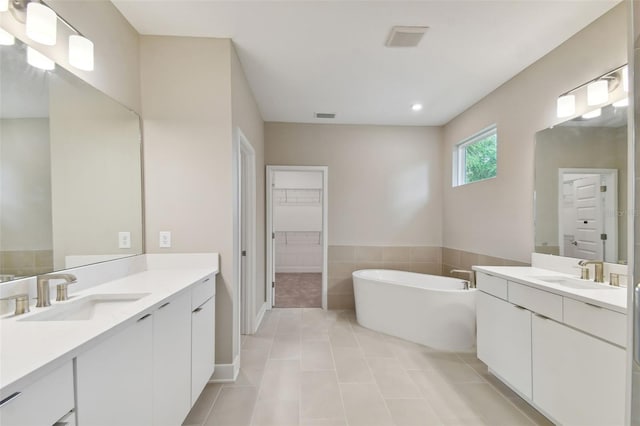 bathroom featuring two vanities, a soaking tub, visible vents, and a sink