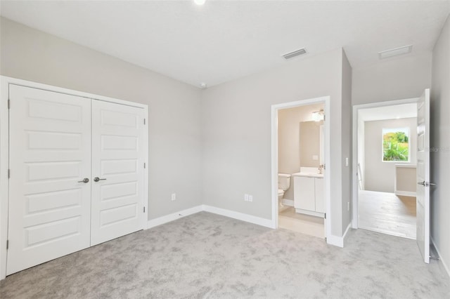 unfurnished bedroom with connected bathroom, carpet floors, visible vents, baseboards, and a closet