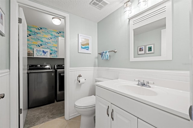 half bath featuring washing machine and clothes dryer, visible vents, toilet, wainscoting, and a textured ceiling