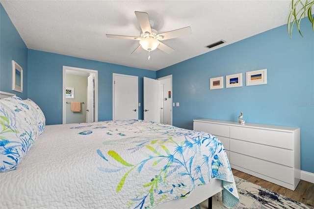 bedroom with visible vents, ensuite bathroom, ceiling fan, a textured ceiling, and wood finished floors