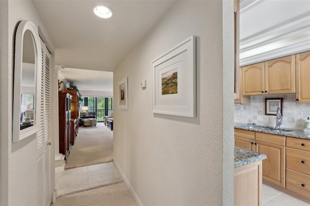 hall featuring light tile patterned floors, baseboards, a sink, and light colored carpet