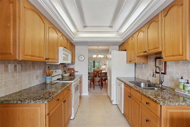 kitchen with white appliances, light tile patterned floors, dark stone countertops, a tray ceiling, and a sink