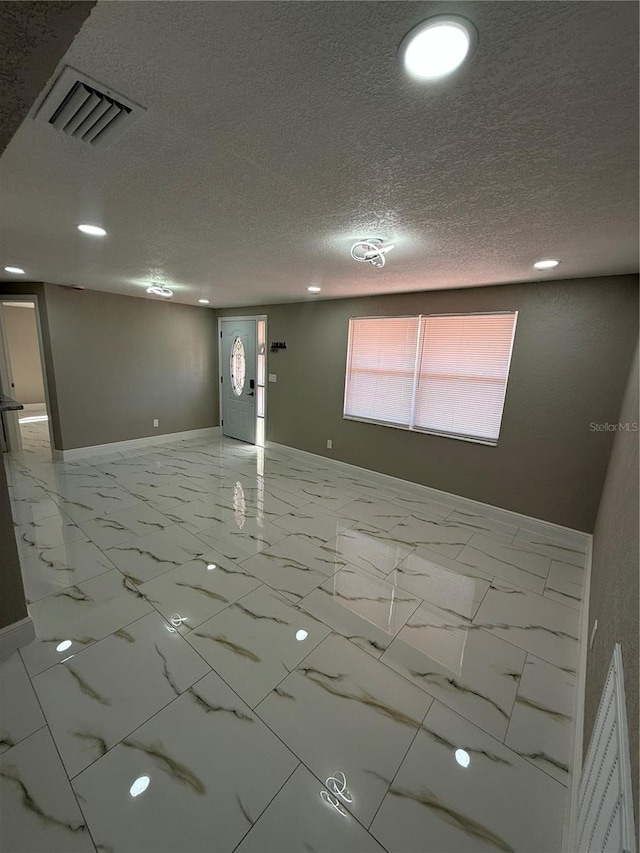 unfurnished room featuring marble finish floor, visible vents, a textured ceiling, and baseboards