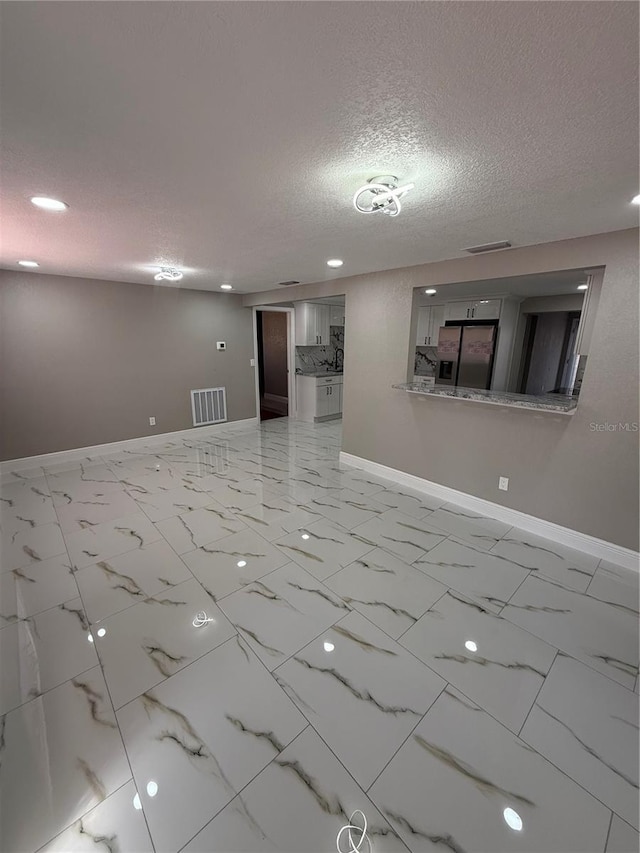 empty room with a textured ceiling, marble finish floor, visible vents, and baseboards