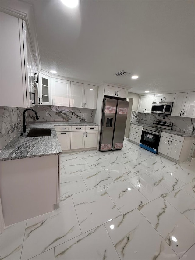 kitchen with appliances with stainless steel finishes, a sink, white cabinets, and light stone countertops