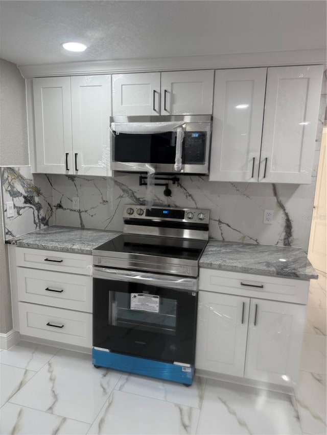 kitchen with marble finish floor, white cabinetry, appliances with stainless steel finishes, and decorative backsplash