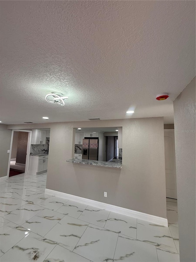 empty room with marble finish floor, a textured ceiling, and baseboards