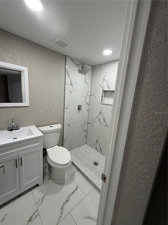 full bathroom featuring marble finish floor, a marble finish shower, a textured wall, toilet, and vanity