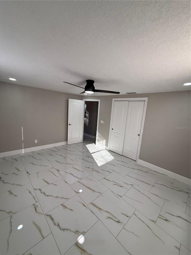 unfurnished room featuring marble finish floor, ceiling fan, baseboards, and a textured ceiling