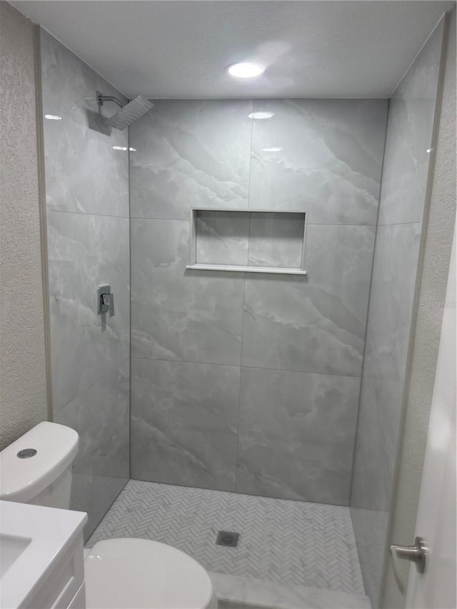 full bathroom featuring toilet, tiled shower, and vanity