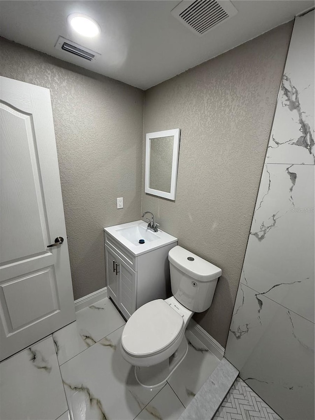 bathroom featuring toilet, visible vents, and a textured wall