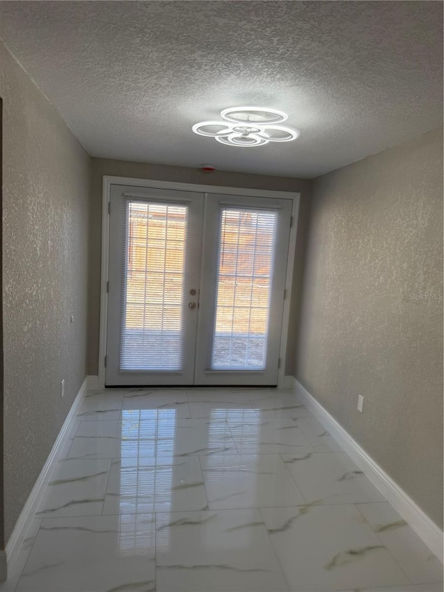 doorway to outside featuring marble finish floor, baseboards, a textured ceiling, and a textured wall