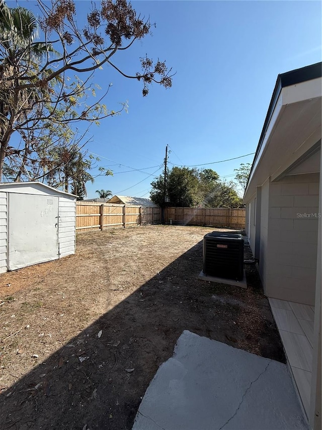 view of yard with a storage shed, a fenced backyard, central AC unit, and an outdoor structure