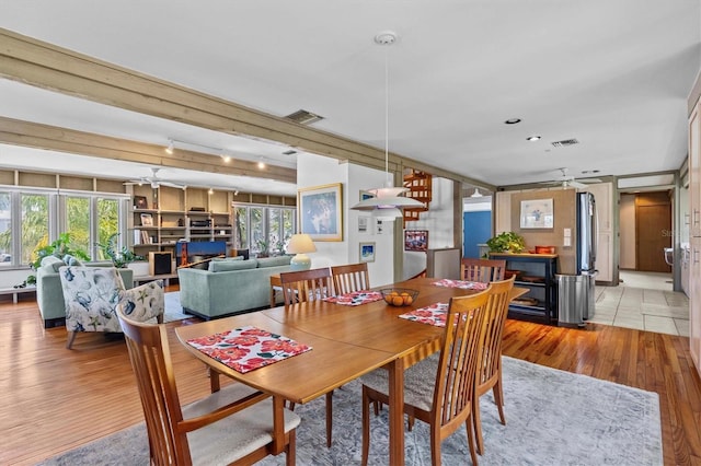 dining space featuring light wood-type flooring, ceiling fan, visible vents, and beamed ceiling