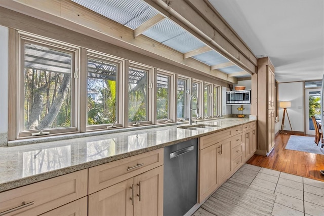 kitchen featuring light stone counters, light brown cabinetry, appliances with stainless steel finishes, a sink, and beamed ceiling