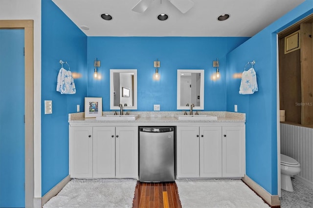 bathroom featuring toilet, double vanity, baseboards, and a sink