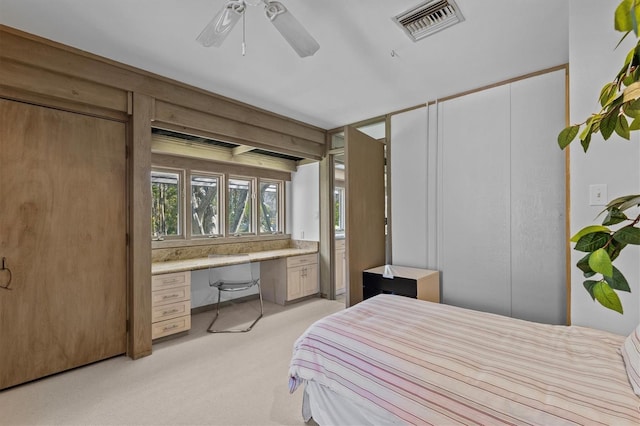 bedroom featuring light carpet, built in study area, visible vents, and a ceiling fan