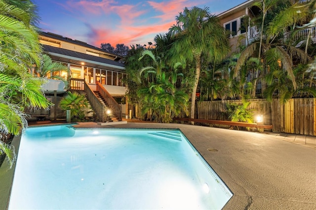 pool at dusk featuring stairs, fence, and a fenced in pool