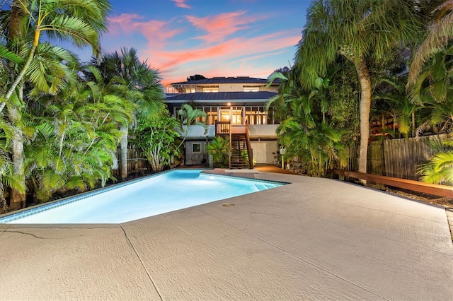 pool at dusk featuring a fenced in pool, a patio, fence, and stairs